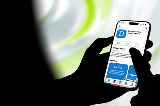 Kiel, Germany - 08-20-2026: Smartphone displaying the Doctolib - Your health partner medical appointment scheduling and healthcare management app in the App Store, held by silhouetted hands with blurr