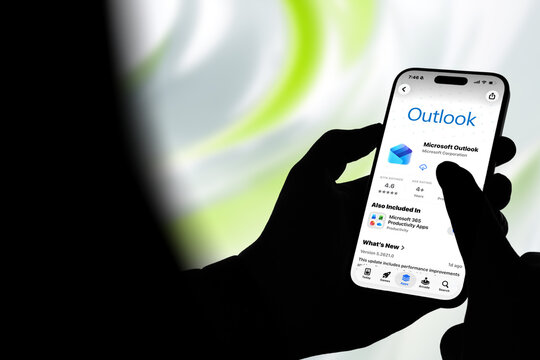 Kiel, Germany - 08-20-2026: Smartphone displaying the Microsoft Outlook email and personal information management app in the App Store, held by silhouetted hands with blurred background