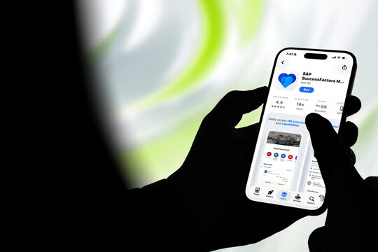 Kiel, Germany - 08-20-2026: Smartphone displaying the SAP SuccessFactors M human capital management and employee experience app in the App Store, held by silhouetted hands with blurred background