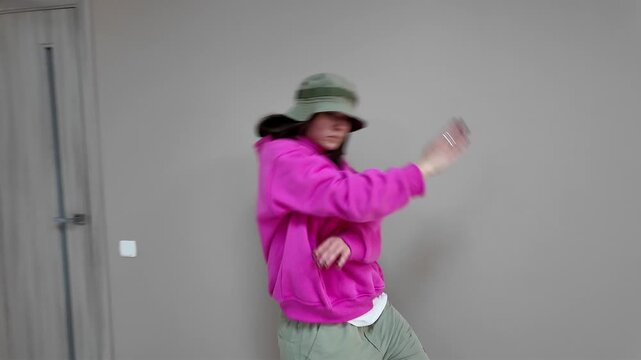 Young Woman in Pink Hoodie and Bucket Hat Dancing Freestyle in a Modern Apartment