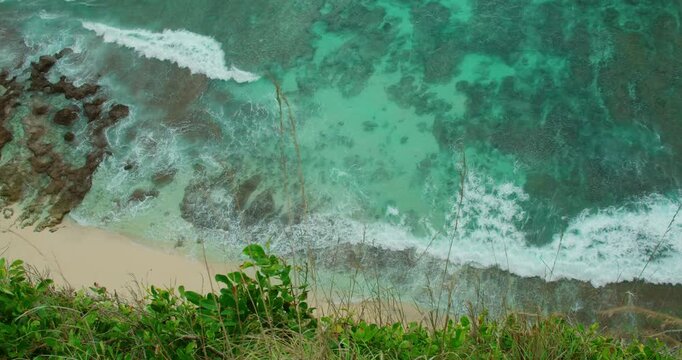 Turquoise ocean waves crash over coral reefs along sandy tropical shoreline in Bali