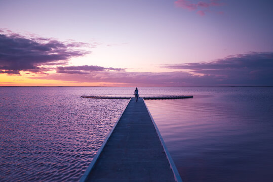 Rear view of a woman walking on a jetty towards an expansive and moody sunset sky, Lake Tyrrell, Victoria, Australia