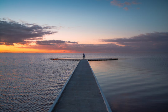 Rear view of a woman standing at the end of jetty surrounded by calm waters, watching an expansive sunset sky, Lake Tyrrell, Victoria, Australia