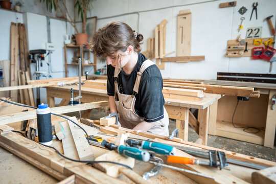 Reconstruction and repair of vintage wooden furniture, woman working at carpentry workshop, talented female woodworker in restoration studio assembling details at workbench using clamps instrument.