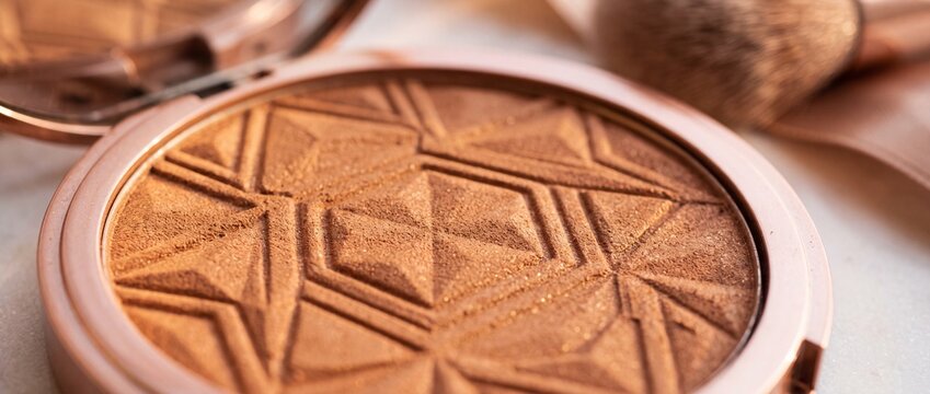 Compact face bronzer with geometric embossed pattern in rose gold case offers warm sun kissed glow for professional beauty styling.