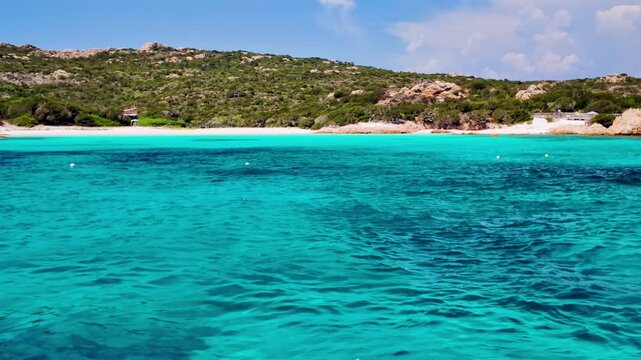 Sunny pink beach, (Spiaggia Rosa) on the island of Budelli over the turquoise clear water of the bay, surrounded by hills covered with Mediterranean vegetation in the La Maddalena archipelago