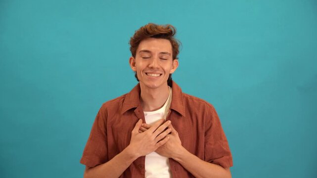 Thankful young man with hands on his chest expressing sincere gratitude on blue background