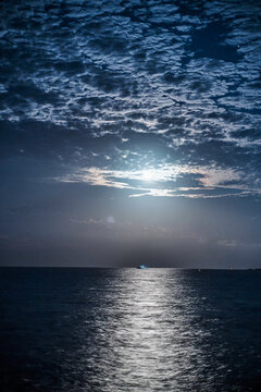 A boat illuminated by moonlight floats on the calm ocean