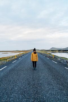 A white woman stands alone on a paved road