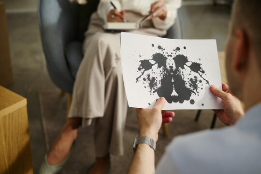 Caucasian man holding Rorschach inkblot test card during therapy session with female psychologist. Image suitable for mental health services and psychological evaluation concepts