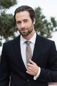 A handsome man elegantly adjusts his black suit jacket on a modern outdoor terrace