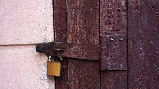 Old brown wooden door locked with a metal padlock on a rusty latch. Concept of safety, security, privacy, and access control. Rustic architectural background.