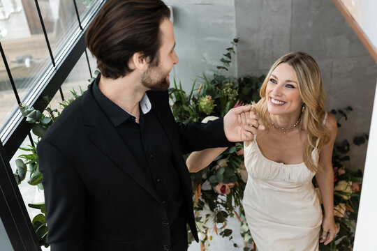 Blonde woman beams as bearded man proposes, surrounded by plants 