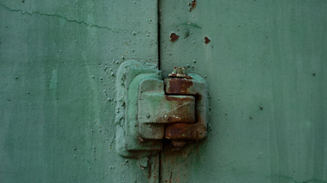 Horizontal closeup of an old rusty metal door hinge on a green painted steel gate. Heavy duty industrial hardware with rust, peeling paint, and aged rough texture for vintage background concepts.