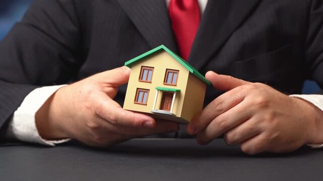 A businessman holds a model of a residential building in his hands. Design and construction. Property valuation and realtor services. House in hand with laptop. Valuation estate