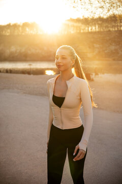 Beautiful woman walking outdoors in athletic wear during warm sunset light. Young woman portrait presents active lifestyle, beauty and skincare, fitness and wellness concept.
