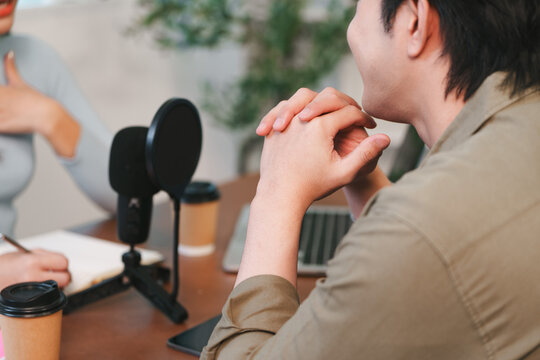 Asian man speaking into microphone during podcast recording with co-host