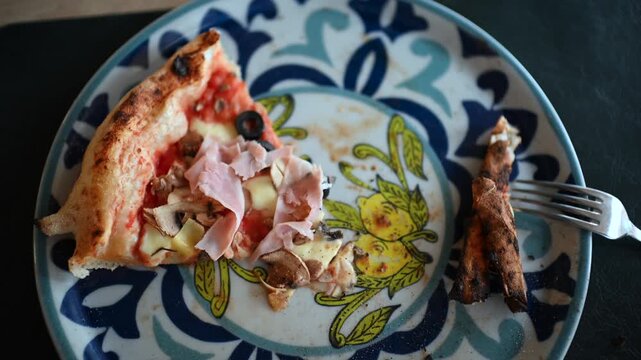 Single slice of delicious ham and mushroom pizza left on decorative patterned plate.