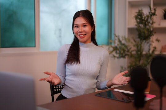 Asian woman hosting video podcast with open gestures in studio