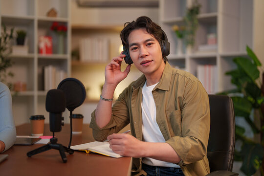 Asian podcast host wearing headphones listening at studio desk