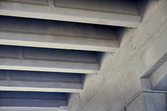 Concrete bridge underside featuring repeating diagonal beams, solid architectural structures, industrial infrastructure support, grey cement perspective textures, transportation engineering layout.