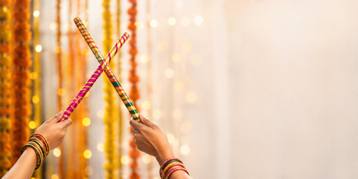 Woman holding crossed colorful dandiya sticks with bangles against festive floral decorations. Navratri celebration background with copy space for greeting card design.