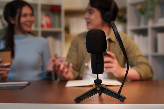 Microphone close up with Asian man and woman recording podcast episode in home studio