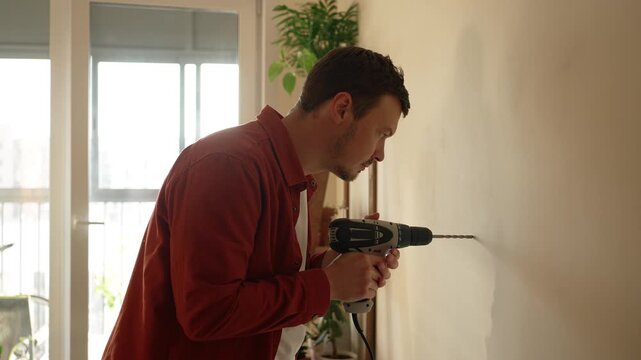 Young man using a power tool for drilling a hole in the wall. Caucasian male homeowner doing do it yourself maintenance, repairing and renovating his new home apartment
