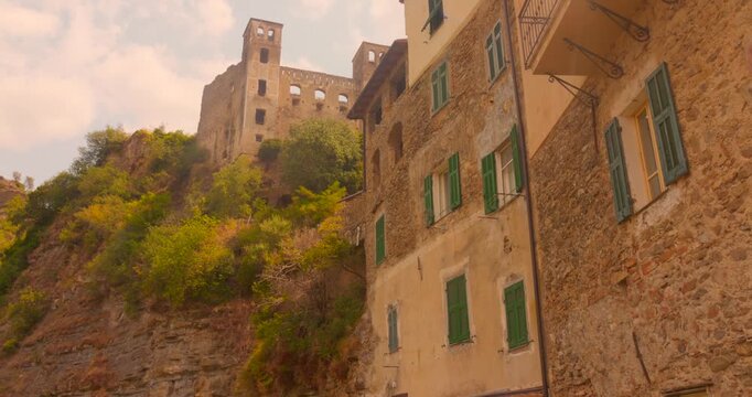 Historic old town stone buildings with green shutters beneath an ancient and medieval Doria Castle tower on a wooded hillside, Dolceacqua, Tuscany, Italy