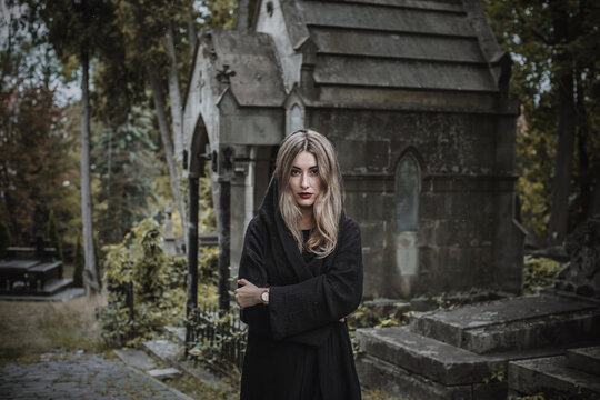 Woman in black hood at old historic cemetery with stone angel statue and ancient crypt, memorial and funerary heritage concept
