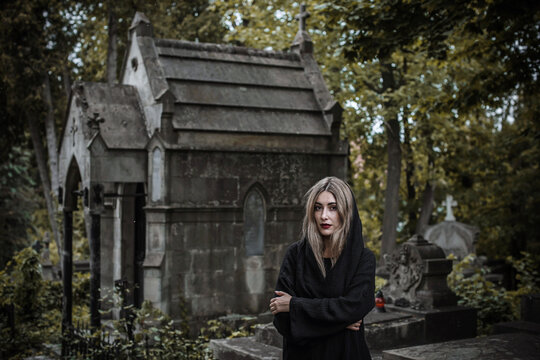 Woman in black hood at old historic cemetery with stone angel statue and ancient crypt, memorial and funerary heritage concept
