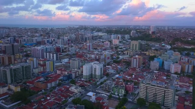 Pullback ascending aerial view over Macei&oacute; to reveal cityscape framed by pink tinted sunset clouds in the sky. Wide angle shot in 4K at 25 fps.