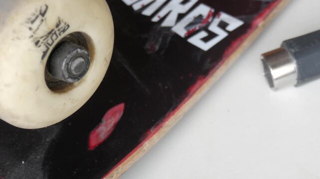 Skateboard wheel and deck on white surface. Skateboard tool next to it.