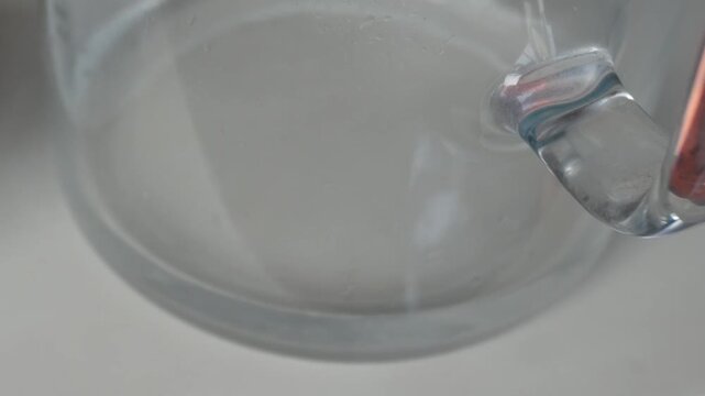Clear glass water filtering jug close up on white surface table. Interchangeable cartridge next to it.