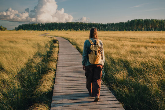 Woman hiking on a wooden boardwalk through open grassland while enjoying ecotourism away from the city