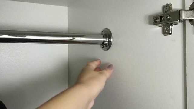 Person testing the strength of a clothes hanging rod in a wardrobe, furniture installation, closet assembly and household storage.