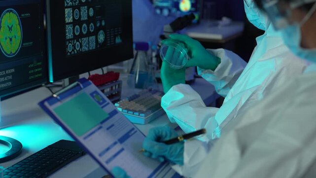 Biomedical researchers wearing PPE kit working with microscope and chemical samples for vaccine development and disease research.