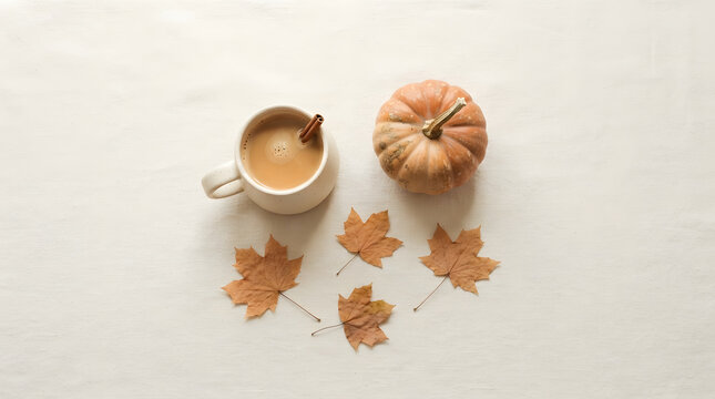 Autumn coffee break with pumpkin and maple leaves on white table setting