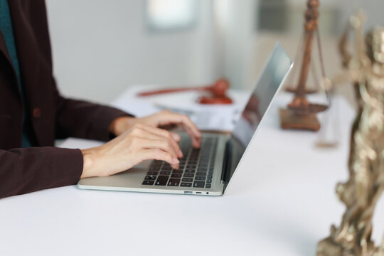 Professional legal expert using a laptop, typing a document in a law office, symbolizing digital justice and online legal services with a gavel and scales of justice on the table