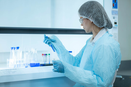 Female scientist examining laboratory tubes working inside a laboratory safety cabinet while conducting sample analysis