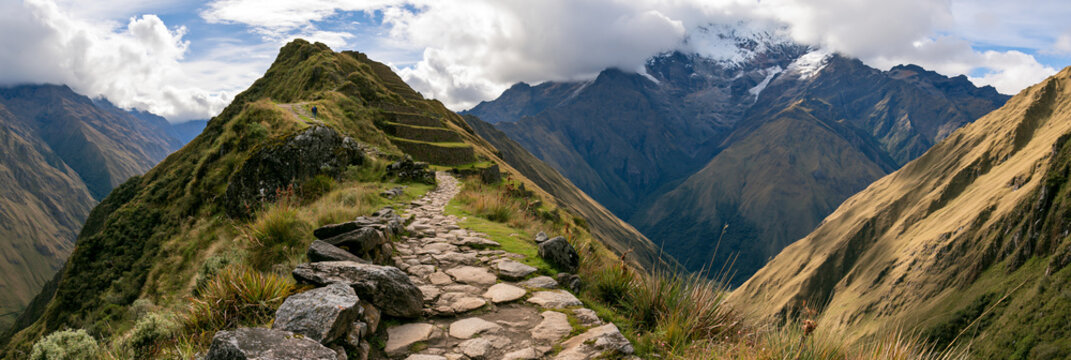 impressive historic inca road winding through the andes, ancient stone path across dramatic mountain terrain, remote inca trail surrounded by terraces and snowcapped peaks