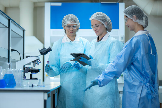 Group of female laboratory researchers analyzing samples with test tubes while using scientific equipment
