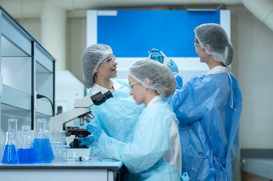 Group of female laboratory researchers analyzing samples with test tubes while using scientific equipment