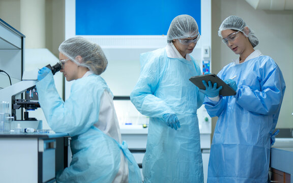 Group of female laboratory researchers analyzing samples with test tubes while using scientific equipment