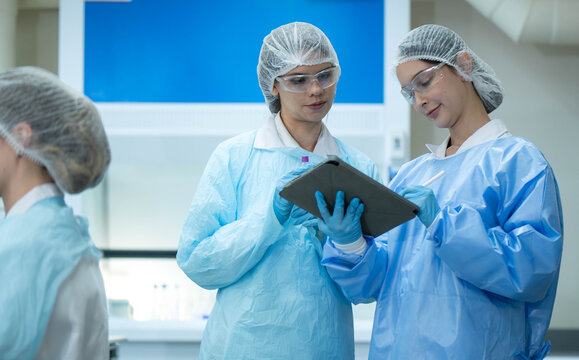 Group of female laboratory researchers analyzing samples with test tubes while using scientific equipment