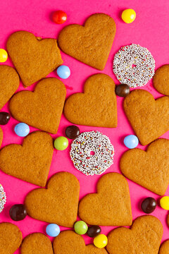 Top view of candies and heart shaped cookies on a vibrant pink background. Dessert photography, sweet treats.