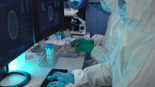 Biomedical researchers wearing PPE kit working with microscope and chemical samples for vaccine development and disease research.