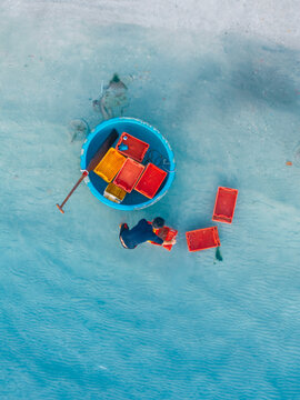 Top down aerial view of a person paddling a round basket boat in turquoise sea at Doc Let beach, Khanh Hoa province, Vietnam