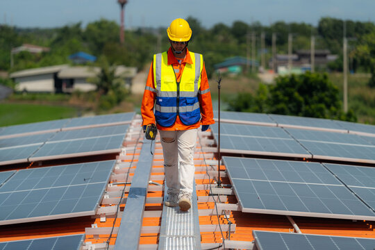 A solar technician walks toward the camera along a narrow rooftop walkway, a lightning rod rising at the end of the walkway - the human side of rooftop renewable energy projects.