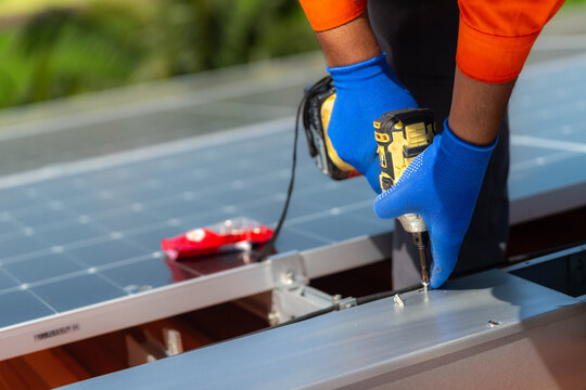 Detail of an installer's hand and drill at a panel clamp on the array, with the array reflecting a bright tropical sky - documenting how commercial solar systems are actually built.